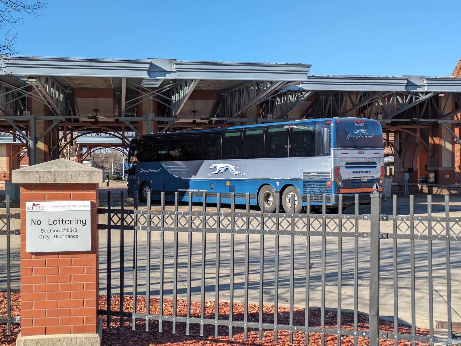 A blue Greyhound bus in the bay at Kalamazoo's train station, next to a No Loitering sign