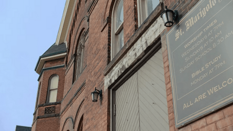 Exterior of brown brick church with a worship times sign posted near the door