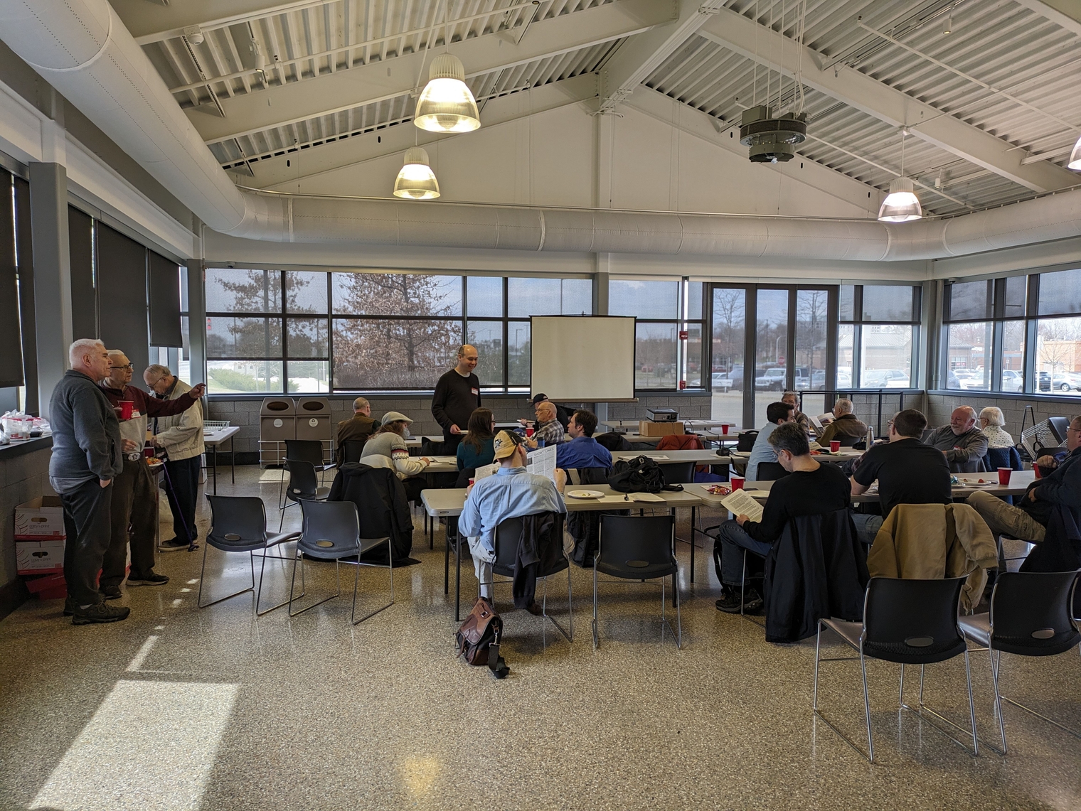 A crowd of 20 to 30 people at tables in front of a projector inside the train station