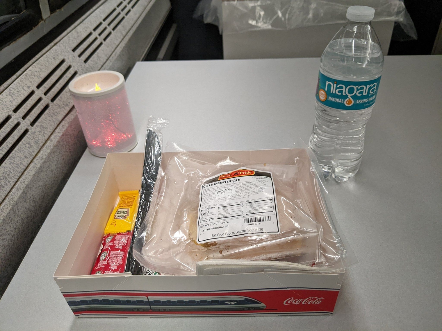 Water bottle and hamburger next to a candle flashing on a table