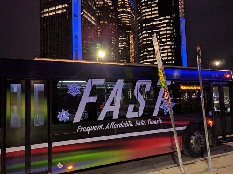 A tie-dye FAST bus decorated in snowflakes at Jefferson and Beaubien in front of the Renaissance Center at night.