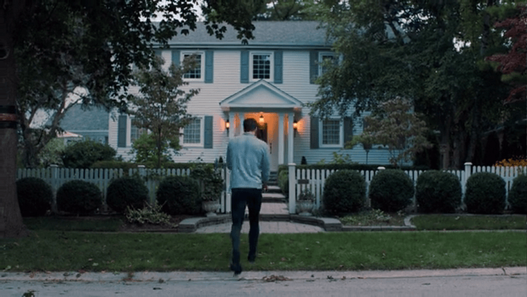 Dodge walking towards his home, a two-story house with white vinyl siding and a picket fence