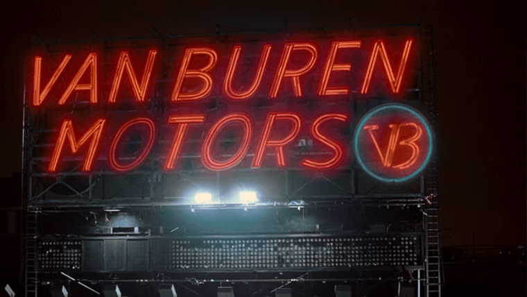 A very large red neon sign atop a warehouse reading “Van Buren Motors”