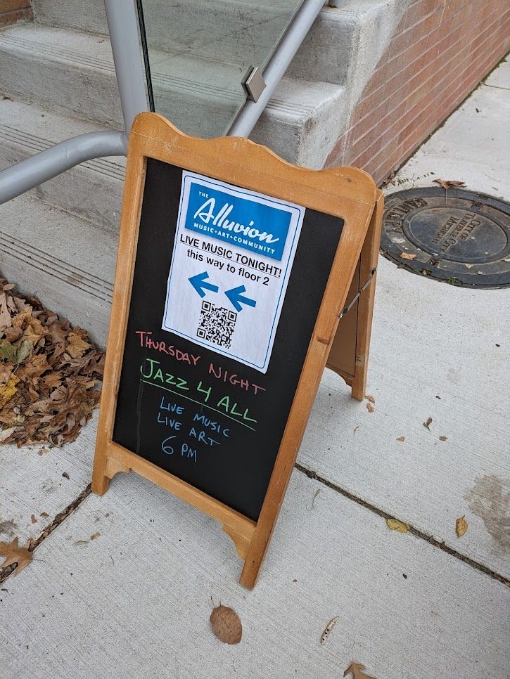 A chalkboard on the sidewalk outside the building advertising a jazz concert on Thursday evening at 6pm.