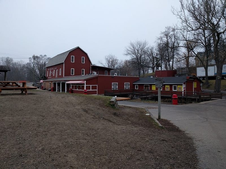 Yates Cider Mill, a red barn with white trim and a water wheel, as seen from a nearby picnic table on an overcast day.