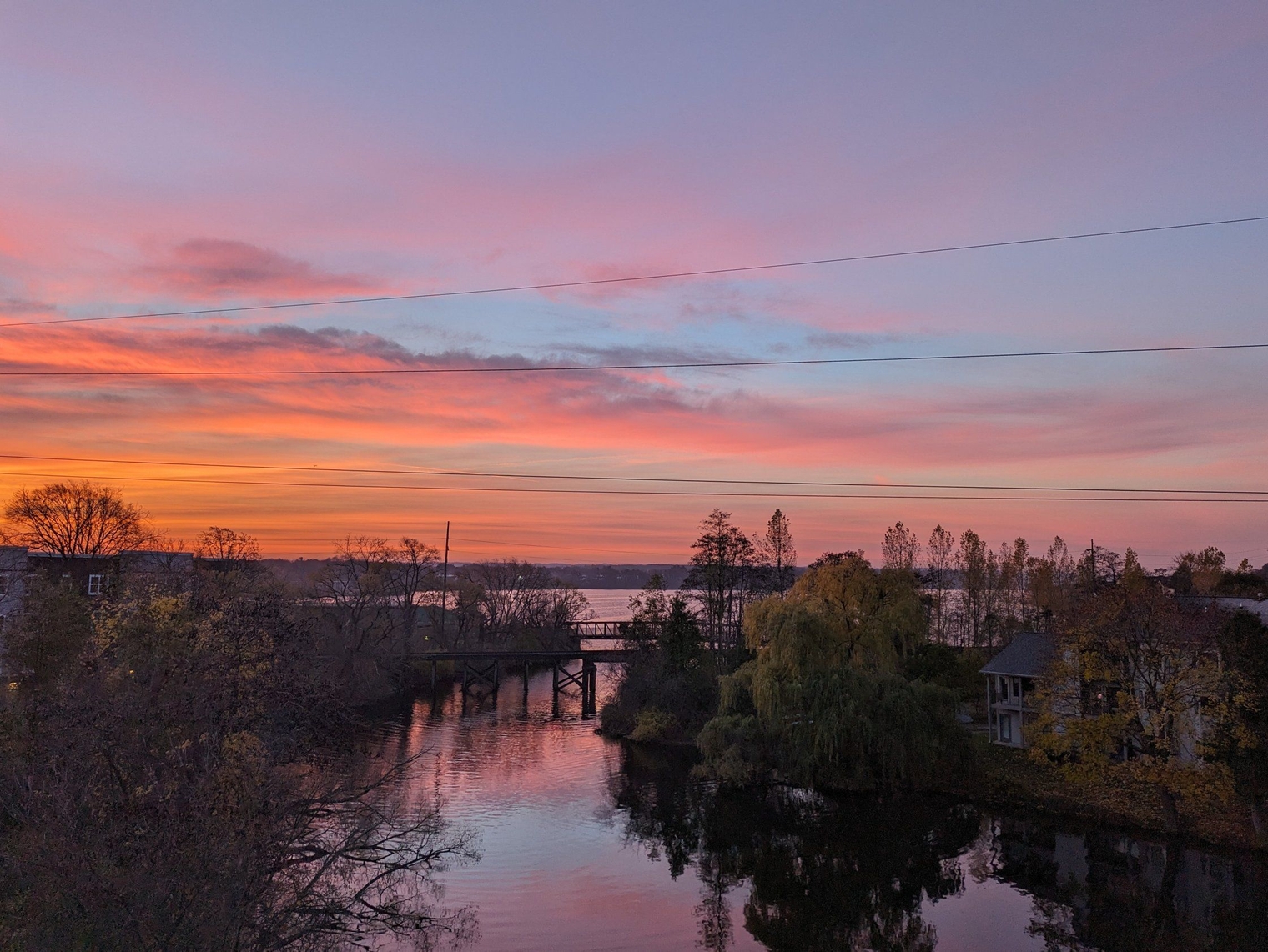 Pink and orange sunrise overlooking the water and a bike trail bridge over the bay