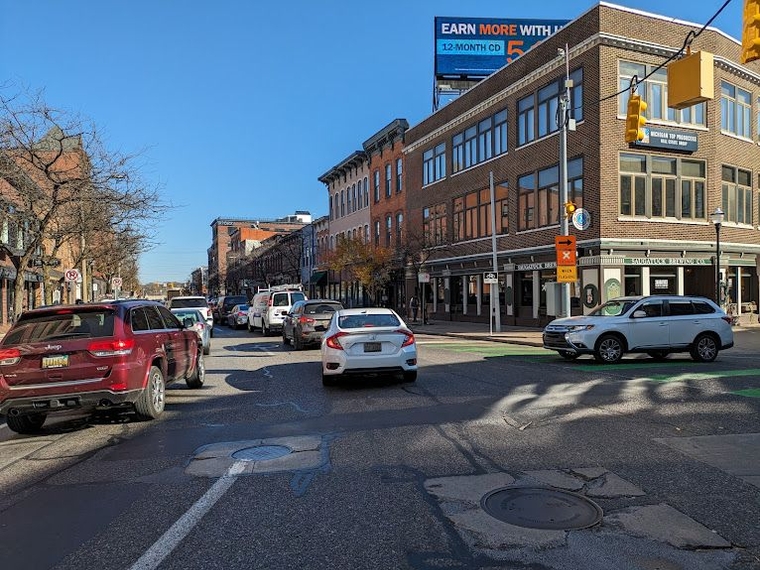 Traffic backed up into an intersection due to a freight train blocking a crossing ahead. A sign is flashing, suggesting drivers follow the planned railroad crossing detour route.