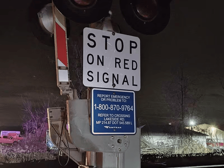 A blue placard with an emergency hotline and grade crossing identification information attached to a crossing arm