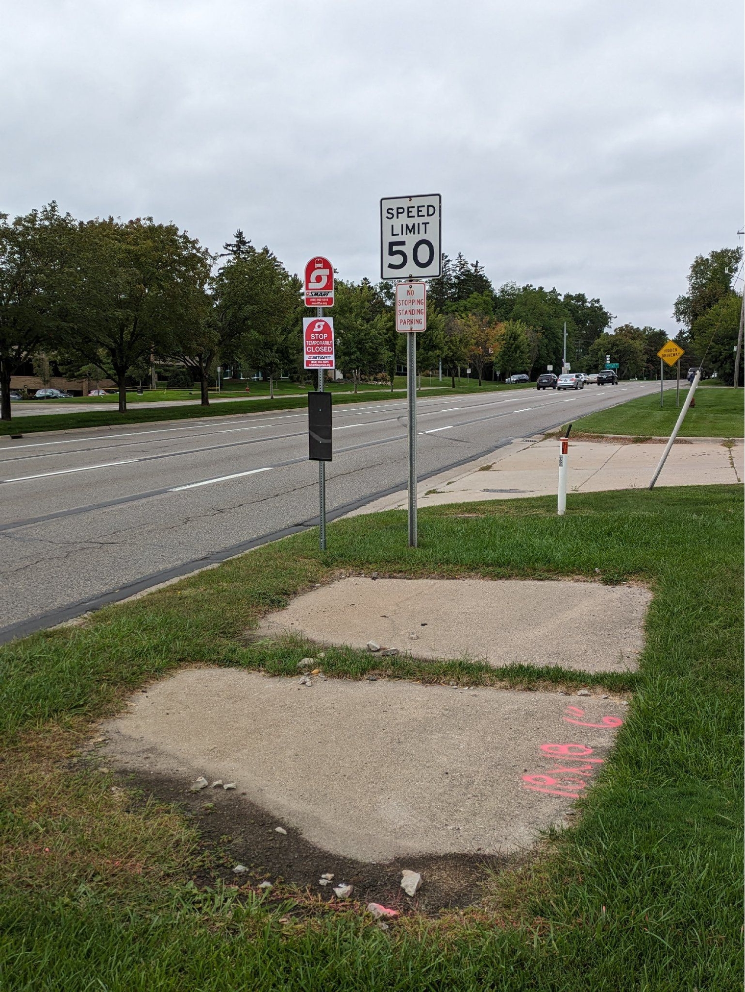 A new SMART sign on Woodward north of Long Lake with a temporary notice that reads "Not in Service." A broken concrete pad surrounded by grass on all sides is the only infrastructure at the stop.