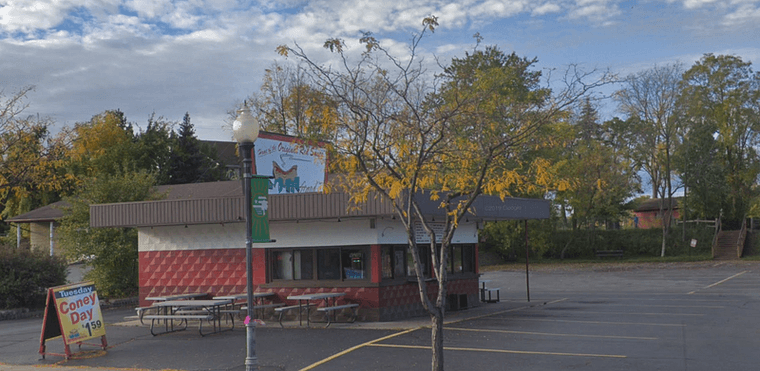 Exterior of Ziggy's, a small shop with two walk-up windows and rows of picnic tables under colorful umbrellas in the parking lot