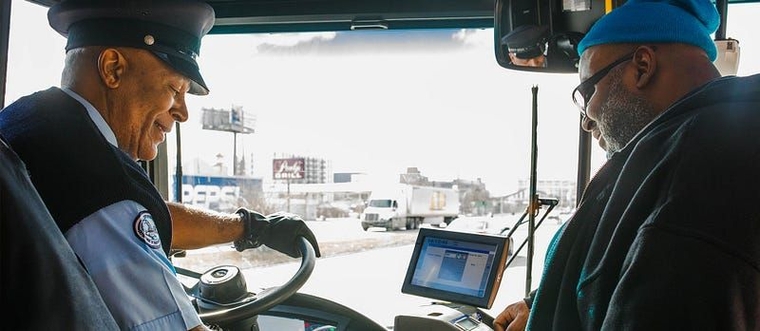 A real bus driver smiling warmly at a boarding passenger