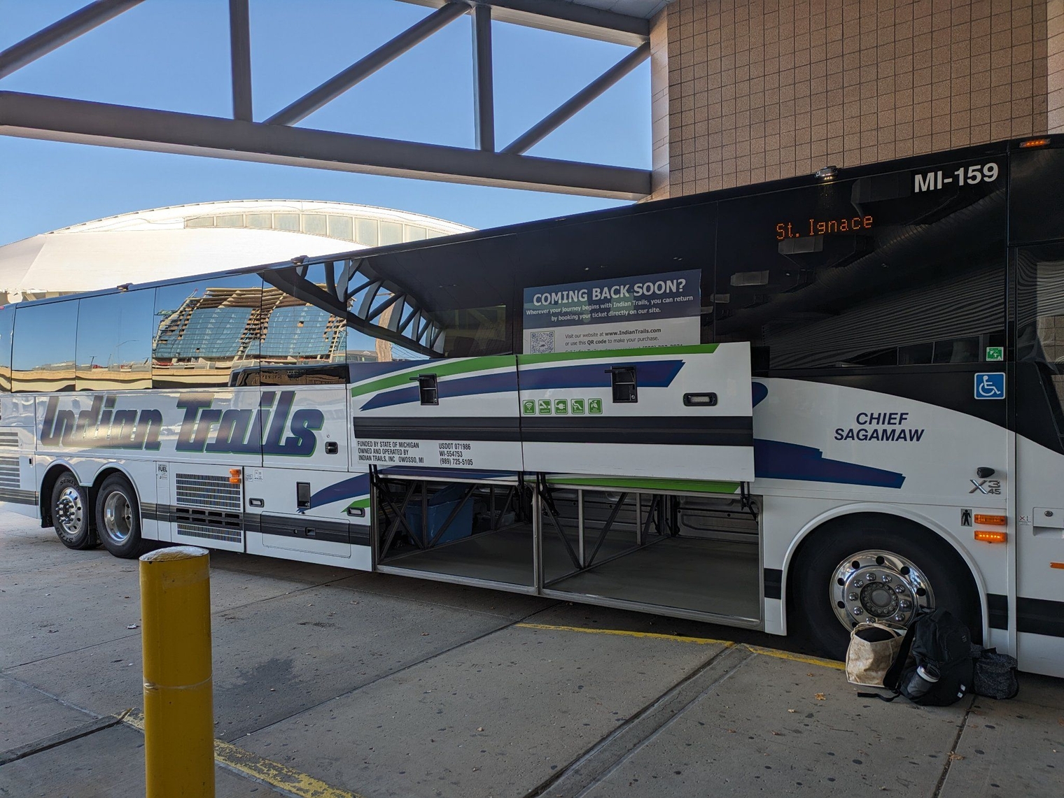 The bus with the luggage doors open, destination St. Ignace