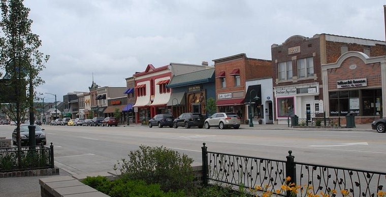 Several prominent buildings in downtown Rochester in the daytime, with parked cars lining the street.