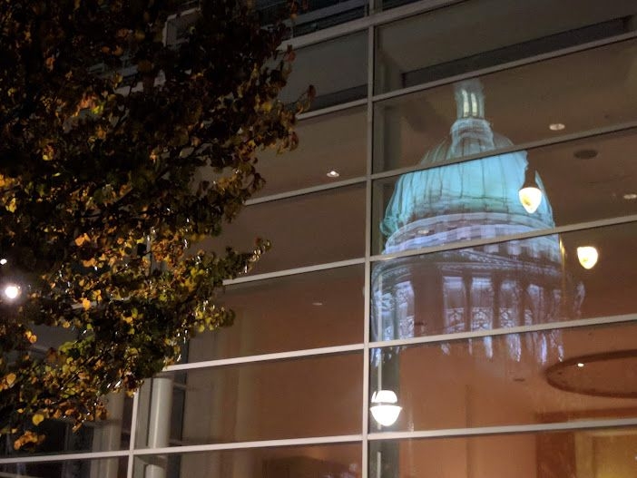 The capitol building at night, reflected in the glass windows of a nearby restaurant