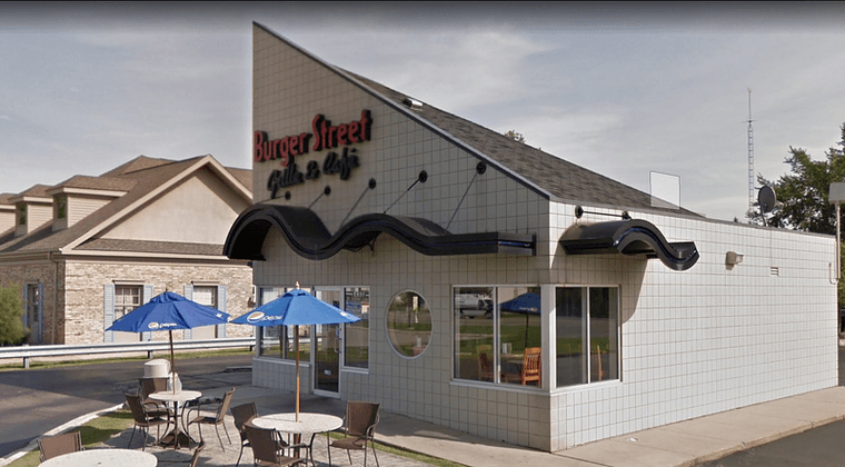 The triangle-shaped building with tiled walls and two tables with umbrellas out front.