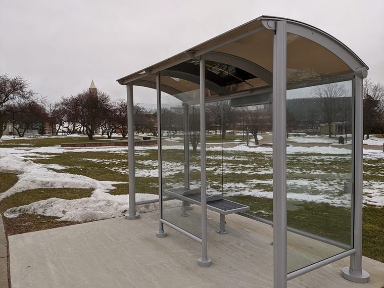 An unmarked bus shelter on a concrete slab next to snow on the ground