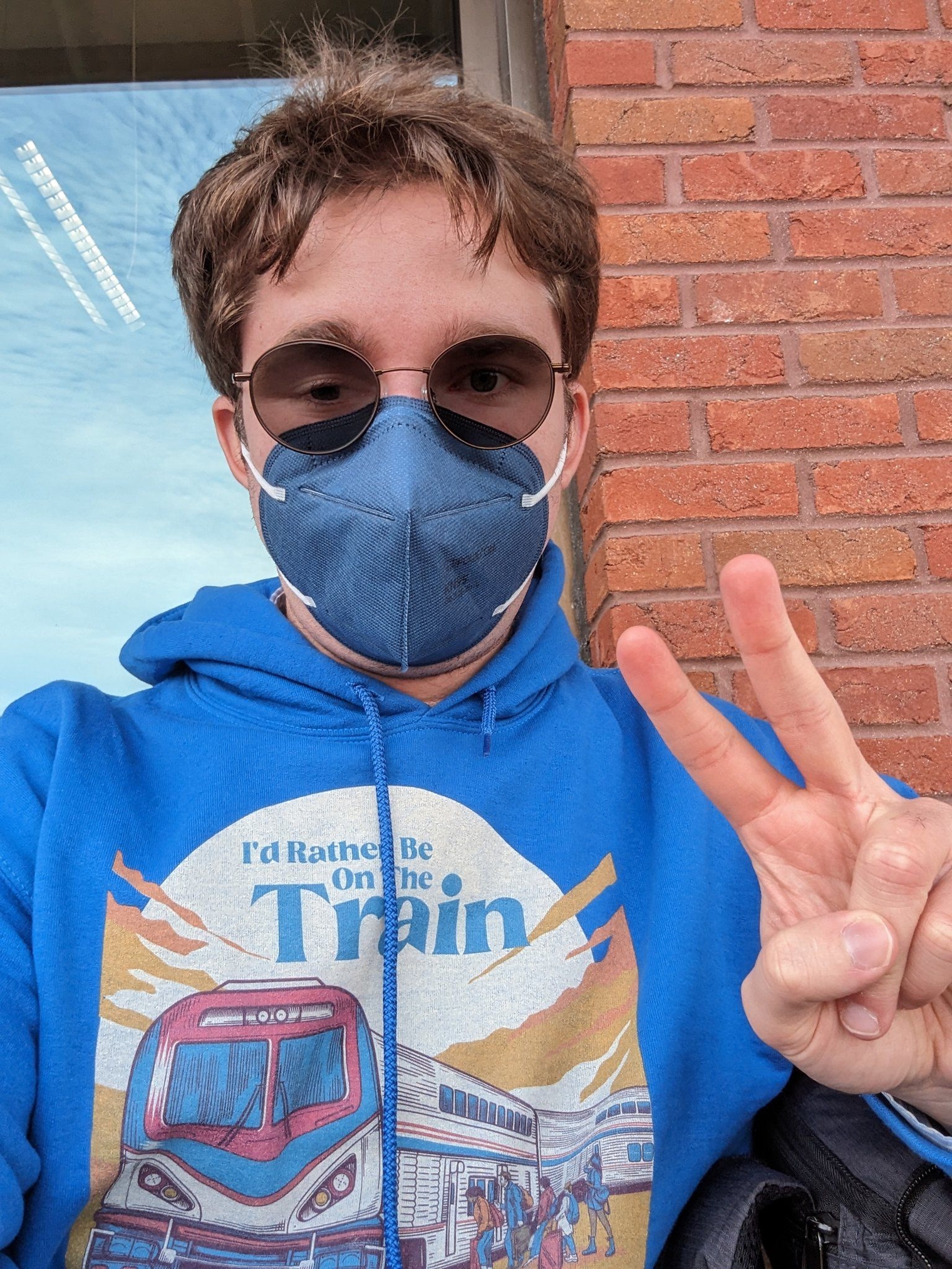 Me wearing my "I'd Rather Be On the Train" sweater, wearing a matching blue mask outside the transit center