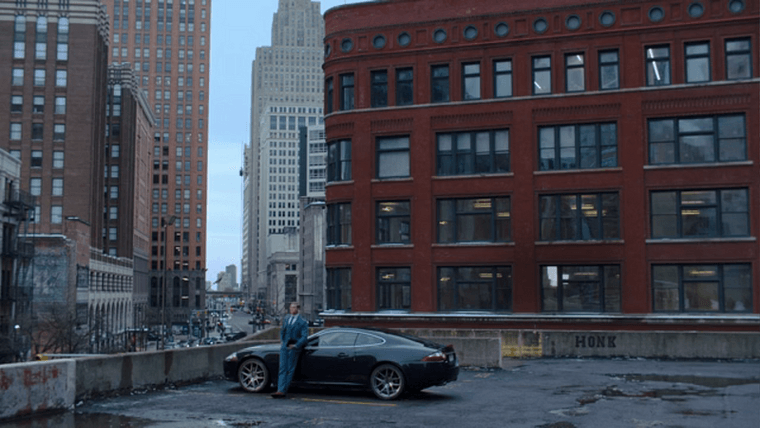 A hunter leaning against a car parked atop a structure overlooking Griswold Street in Detroit