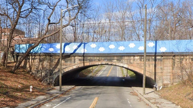 Old stone arch bridge in southwest Detroit, with a rebuilt safety wall painted blue with white clouds