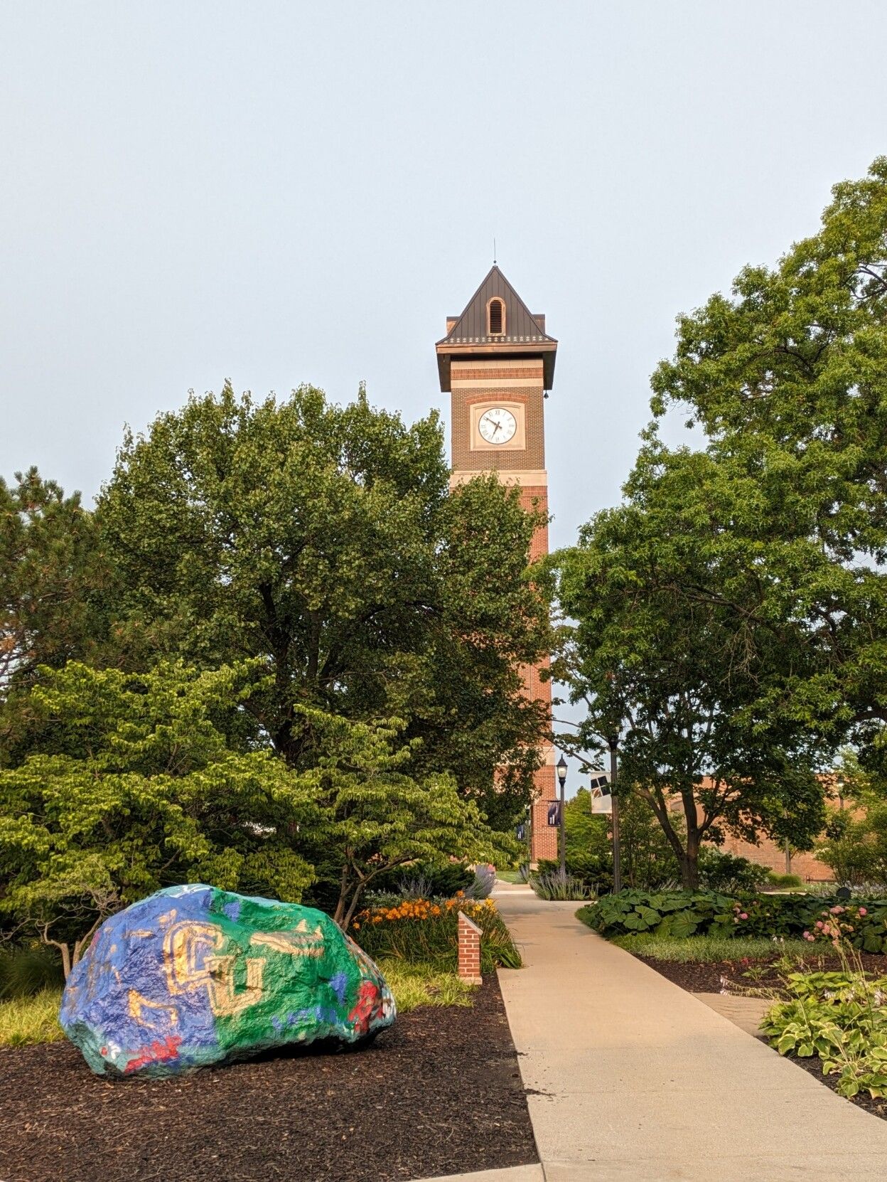 Campus clock and painted rock in purple and green with the university's letters