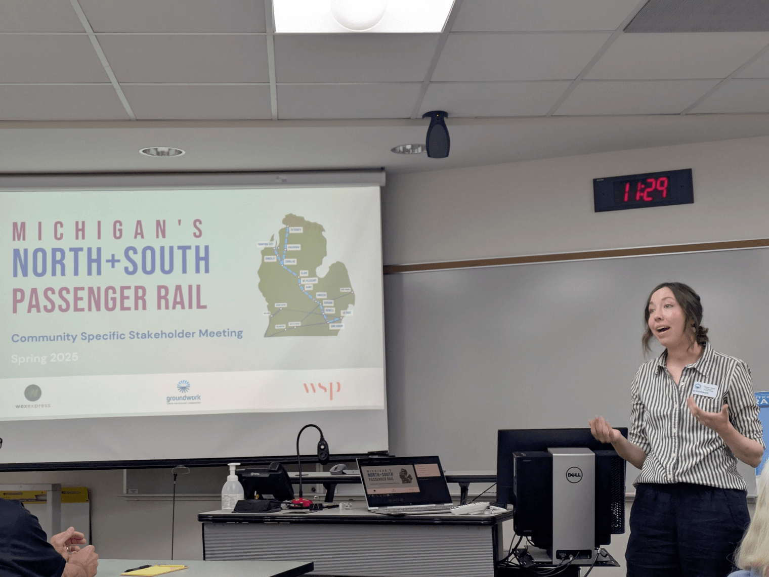 Carolyn Ulstad of the Groundwork Center addresses meeting attendees in front of a projector slide reading "Michigan's North+South Passenger Rail: Community Specific Stakeholder Meeting, Spring 2025".