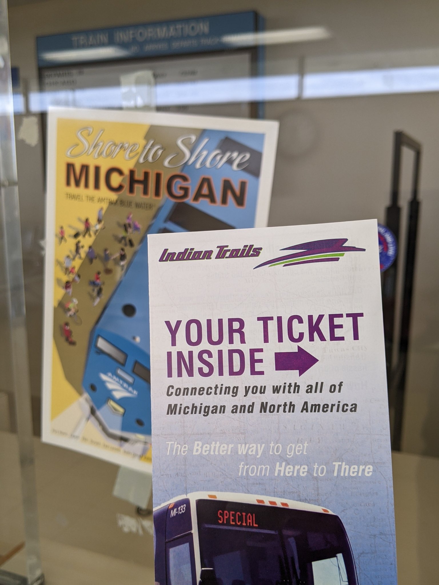 An Indian Trails ticket envelope held up next to an Amtrak Blue Water flyer on the ticket window