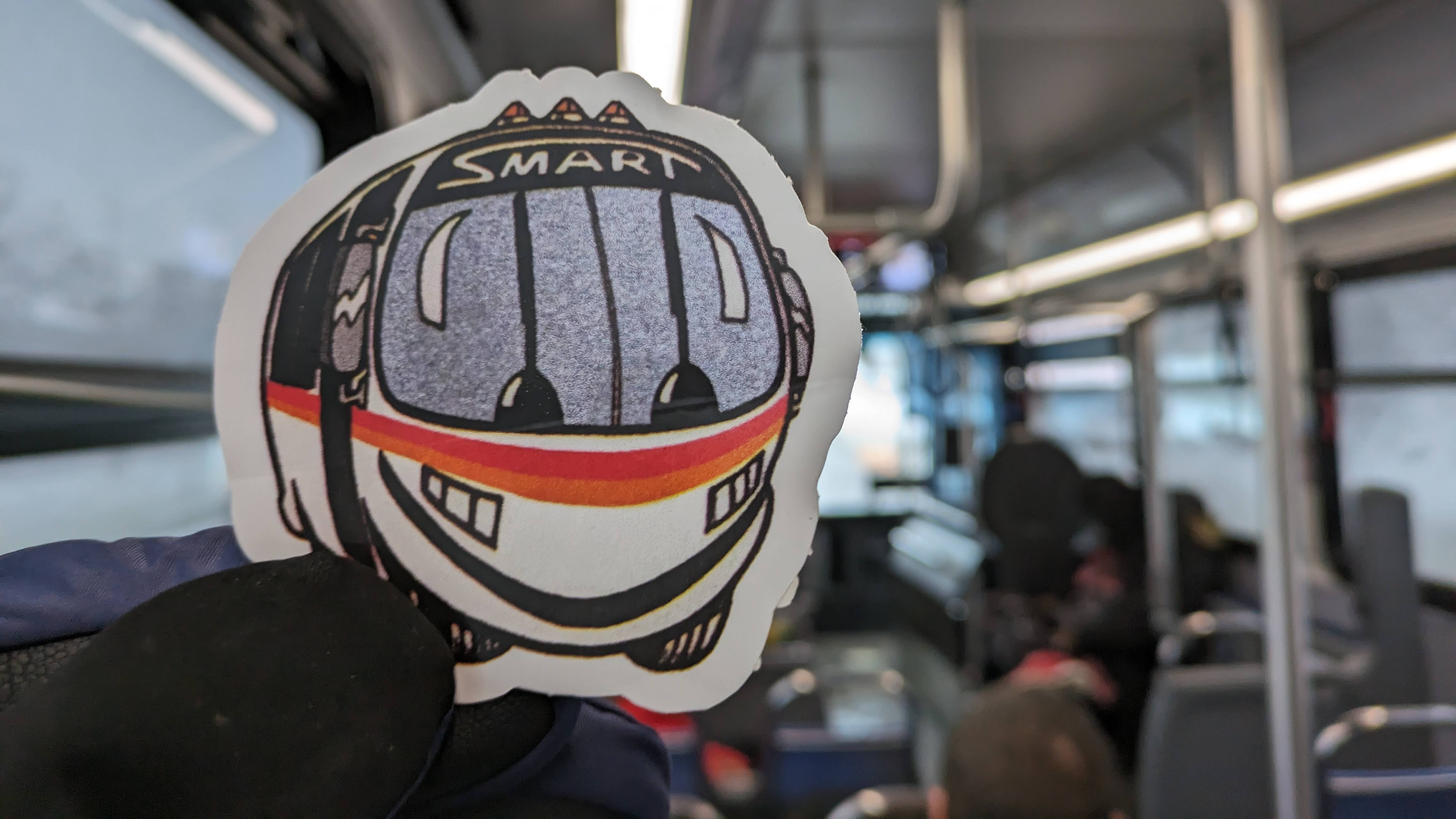 Me holding up a Smartie sticker, SMART's old anthropomorphic mascot from the 90s, on a FAST bus.