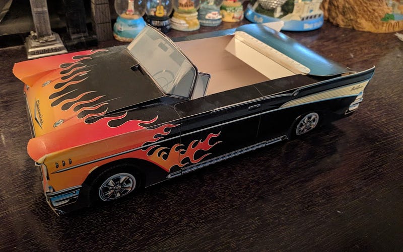 A paper food tray shaped like a black Chevy Bel Air with orange flames on the hood