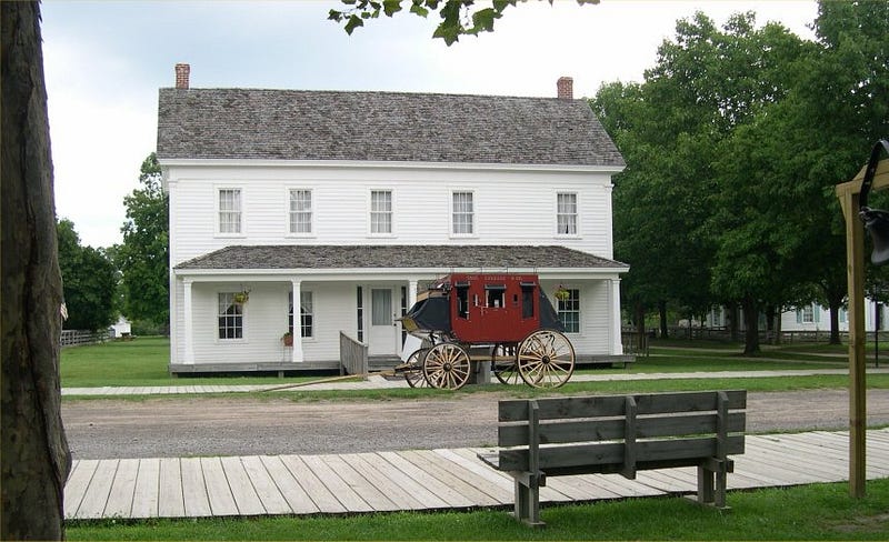 A white two-story tavern with a horse-drawn carriage out front