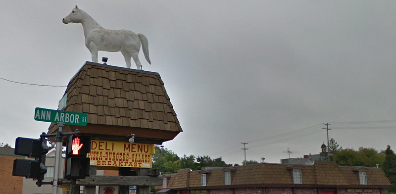 A white statue of a horse atop the sign for the tavern which reads "Deli Menu, Pizza, Burgers, Salads, Breakfast"